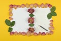 Double frame of dried rose petals on a white and yellow background with a sheet of paper and a pencil for your text