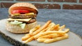 Double juicy cheeseburger with french fries, lettuce, tomato, cheddar cheese front of vintage brick wall