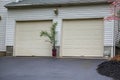 Double overhead garage doors with a potted palm tree in between the doors at the end of as asphalt driveway. Royalty Free Stock Photo
