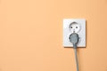Double power socket with inserted plug on pale orange wall, space for text. Electrical supply Royalty Free Stock Photo