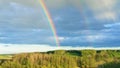 Double rainbow as a rare natural phenomenon against the backdrop of a hilly rural landscape. Bright real rainbow over the forest Royalty Free Stock Photo