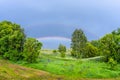 Double rainbow in the blue cloudy sky over green meadow and a forest illuminated by the sun in the country side Royalty Free Stock Photo