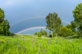 Double rainbow in the blue cloudy sky over green meadow and a forest illuminated by the sun in the country side Royalty Free Stock Photo