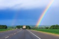 Double rainbow in the blue cloudy dramatic sky over green field and a road illuminated by the sun in the country side Royalty Free Stock Photo