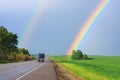 Double rainbow in the blue cloudy dramatic sky over green field and a road illuminated by the sun in the country side Royalty Free Stock Photo