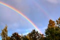 Double rainbow in the blue sky over the forest on a summer day