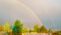 Double rainbow after rain over the roofs of rural houses and flowering trees on a spring or summer day. A beautiful natural Royalty Free Stock Photo