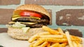 Delicious double tasty hamburger with beef cutlet, french fries, fresh vegetables and 2 slices of cheddar cheese on vintage wooden Royalty Free Stock Photo