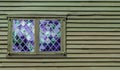 Double window with purple panes in a diamond pattern in the wall of a colonial building Royalty Free Stock Photo