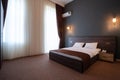 Double wooden bed, with white pillows, bedside tables on the sides, against the blue wall with lamps.