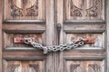 A double wooden door chained closed. Closeup of old wooden door with closed padlock on a chain. A chain of silver color Royalty Free Stock Photo