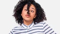 Doubtful African American young woman, looking aside with curious face, dressed in casual striped shirt, posing over white wall.