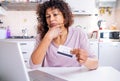 Doubtful black woman using credit card for online shopping