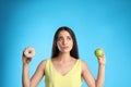 Doubtful woman choosing between apple and doughnut on light blue background Royalty Free Stock Photo