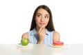 Doubtful woman choosing between apple and doughnut at table on white background Royalty Free Stock Photo