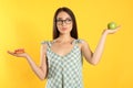 Doubtful woman choosing between apple and doughnut on yellow background Royalty Free Stock Photo