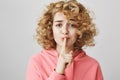 Doubtful worried curly-haired woman with cute face making shush gesture, holding index finger on mouth, being anxious Royalty Free Stock Photo