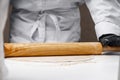The dough ball is rolled out with a wooden rolling pin by a man in black gloves. Close up Royalty Free Stock Photo