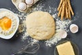 Dough with flour near different utensils and ingredients lies on dark concrete table. Baking process