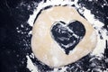 A dough heart on the table. An overhead photo of some flour, wheat dough and cookie cutter like a heart shape.