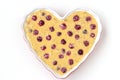 Dough for oatmeal cake with cherries in ceramic form in the shape of a heart on a white background