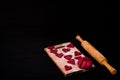 Dough and raw red heart-shaped cookies on wooden board with flour, wooden rolling pin. Black table Royalty Free Stock Photo