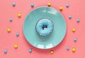 Doughnut with blue icing on a blue plate on a pink background.