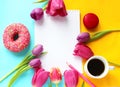 Doughnut, coffee, Notepad and bright tulips on a blue and yellow background.