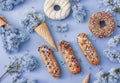 Doughnuts and cream cakes lie on the table among lilac flowers on blue paper. Spring and sweets, delicious cakes. Still life and Royalty Free Stock Photo
