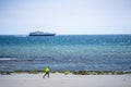 Douglas, Isle of Man. Man running at the beach with cruise ship close to shore. Powerful runner training outdoor on summer