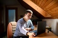 Down syndrome adult man sitting indoors in bedroom at home, using laptop. Royalty Free Stock Photo