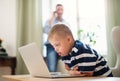 Down syndrome boy with unrecognizable father indoors at home, using laptop.