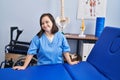 Down syndrome woman wearing physiotherapy uniform leaning on massage table at physiotherapist clinic Royalty Free Stock Photo