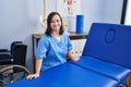 Down syndrome woman wearing physiotherapy uniform leaning on massage table at physiotherapist clinic Royalty Free Stock Photo