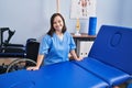 Down syndrome woman wearing physiotherapy uniform leaning on massage table at physiotherapist clinic Royalty Free Stock Photo