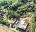 Downsized plant for the repair of machines with a scrap yard behind a forest with a wild dump, diagonally shot aerial photograph.