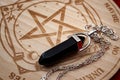 Dowsing pendulum with black gemstone next to hardwood divination chart on red velvet backgrounds concept for mystic magic spell, Royalty Free Stock Photo