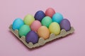 A dozen colored Easter chicken eggs in a cardboard package on a pink background