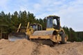 Dozer and Vibro Roller Soil Compactor at road construction and bridge projects in forest area. Heavy machinery for road work.