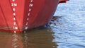 Draft mark numbers on red steel hull surface of nautical vessel while docked at shipyard area