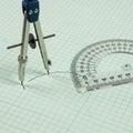 Drafting tools, including a metal compass and a plastic protractor, are placed on graph paper with Royalty Free Stock Photo
