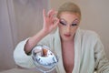 Drag queen person removing false eyelashes and wearing bathrobe.
