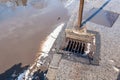 Drainage or sewage manhole grid system on the street asphalt road useless because of damaged tarmac with pot hole full of water af Royalty Free Stock Photo