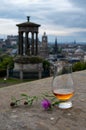 Dram glass of single malt scotch whisky and view from Calton hill to park and old parts of Edinburgh city in rainy day, Scotland,