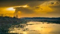 Dramatic autumn orange sunset reflected on the surface of the water in a narrow river with marshy grassy banks