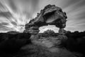 A dramatic black and white landscape photograph of an incredible rock arch