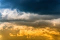 Dramatic blue thunderclouds on top and yellow-golden fluffy clouds illuminated by rays of sun on below Royalty Free Stock Photo