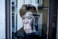 Dramatic close up portrait of young beautiful woman thinking and feeling sad suffering depression at home window looking depresse Royalty Free Stock Photo