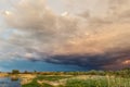 Dramatic dark cloudy thunder sky over dry grass field at pond shore. Rural countryside rainy ominous cloudscape over dry autumn Royalty Free Stock Photo