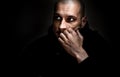 Dramatic dark portrait with strong contrast and film grain of young man sitting in the room with sadness and depression in his eye